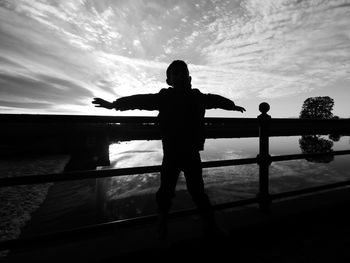 Silhouette man standing by railing against sea during sunset