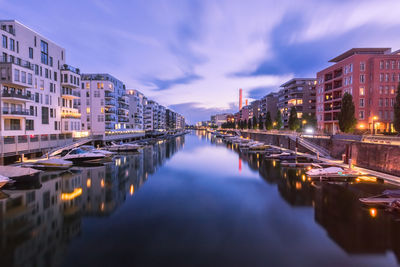 River amidst illuminated buildings against sky at dusk