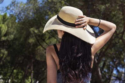 Rear view of woman wearing hat standing against trees