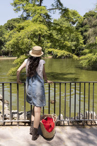 Rear view of woman with hat on railing against trees