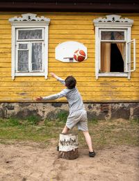 Rear view of kid playing basketball near house