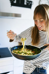 Young woman holding pan with vegan pasta dish