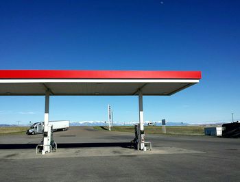 Gas station by road against clear blue sky