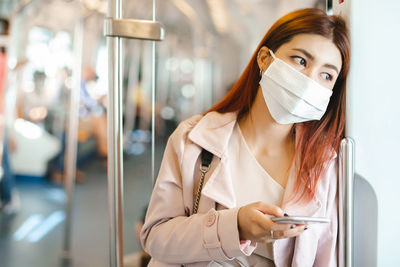 Asian women passengers wearing medical face masks holding smartphones in subway train system public.
