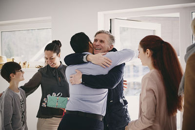Smiling senior father embracing man while standing by family at doorway