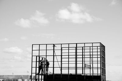 Men working on metallic built structure against sky
