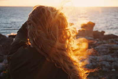 Rear view of woman with tousled hair standing on shore during sunset