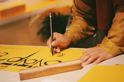 Midsection of man writing on yellow paper