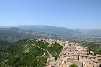 Aerial view of townscape by mountains against clear blue sky