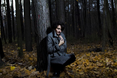 Young woman sitting on tree trunk in forest during autumn