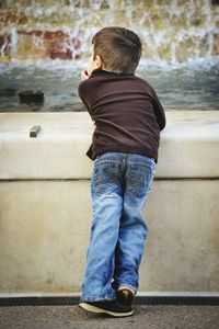 Boy leaning on wall against fountain