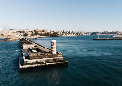 Lighthouse on pier in sea against clear sky