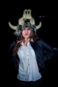 Portrait of angry young woman wearing animal skull on head over black background