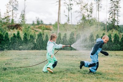 Sister spraying her brother with a hose whilst playing in the rain