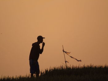 Silhouette man standing on field against sky during sunset