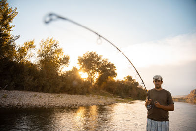 Portrait of man fishing in river against sky