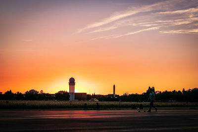 Man with skateboard walking in city against orange sky