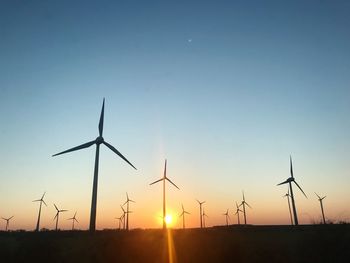 Wind turbines on field against clear sky during sunset
