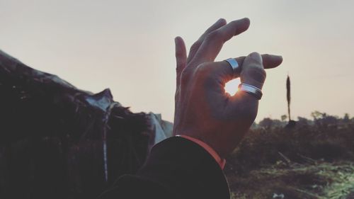 Optical illusion of hand holding sun against sky during sunset