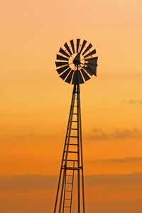 Low angle view of silhouette traditional windmill against orange sky