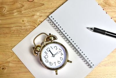 Directly above shot of alarm clock and pen on spiral notebook