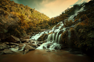 Scenic view of waterfall in forest against sky