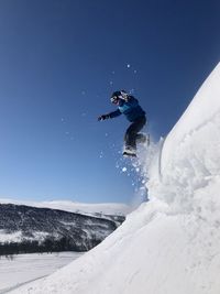 Boy jumping in snow against clear sky