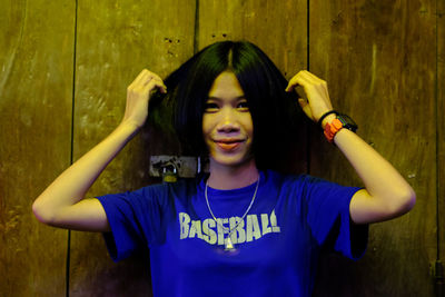 Portrait of smiling young woman standing against wooden wall