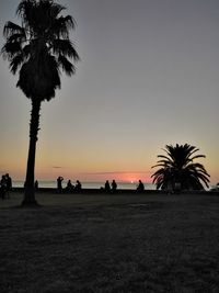 Silhouette palm trees on beach against clear sky at sunset