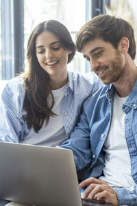 Portrait of smiling friends using laptop at office