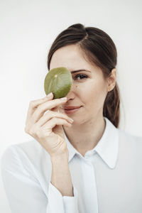 Elegant businesswoman holding leaf on her eye against white background in studio