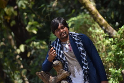 Young man holding toy gun while standing against trees