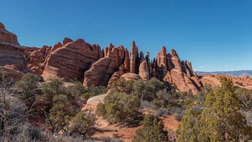 Panoramic view of rugged terrain and rock formations against clear blue sky 