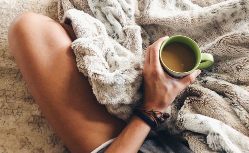 Midsection of woman having coffee on bed