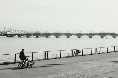 Man cycling on railing by sea against clear sky