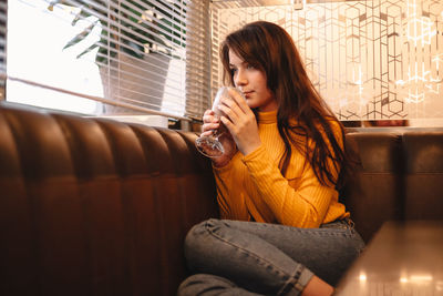 Thoughtful young woman drinking chocolate milkshake in cafe by window