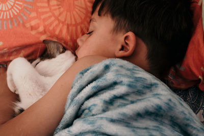 High angle view of boy with cat sleeping on bed