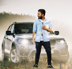 Young man standing by car against sky