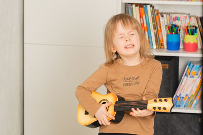 Funny child at home learning to play the guitar. portrait of a child with closed eyes smiling