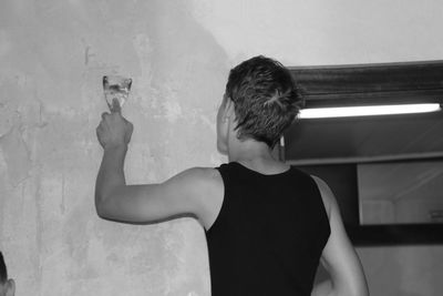 Rear view of young man plastering wall with scraper