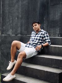 Portrait of young man sitting on staircase against wall