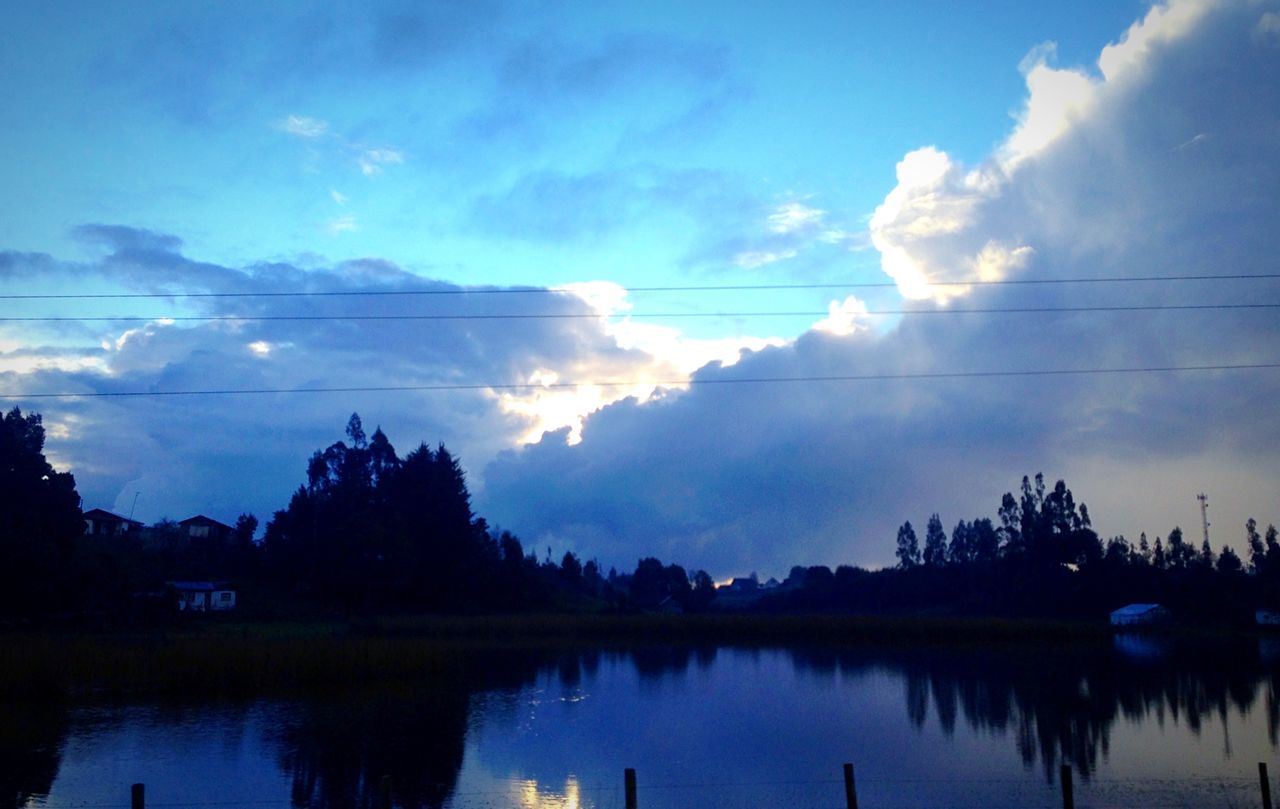 tranquil scene, silhouette, tranquility, tree, scenics, lake, water, reflection, sky, beauty in nature, nature, calm, cloud - sky, non-urban scene, blue, cloudscape, majestic, tourism, waterfront, growth, outline, dark, outdoors, standing water, day, no people, vacations, power line, reflection lake