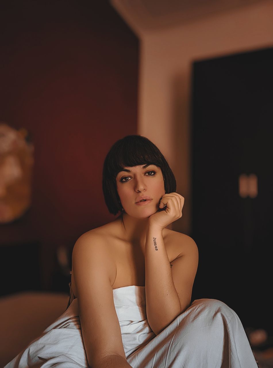sitting, indoors, one person, young adult, lifestyles, portrait, three quarter length, looking at camera, focus on foreground, beauty, front view, women, young women, furniture, real people, beautiful woman, bed, adult, clothing, hairstyle, contemplation