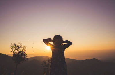 Silhouette man standing on rock against sky during sunset