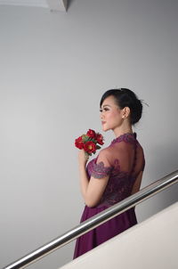 Side view of smiling woman holding red roses while standing by railing