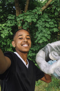 Portrait of smiling teenage boy taking selfie with garbage bag