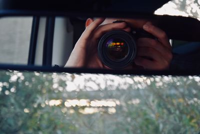 Man photographing while reflecting on rear-view mirror