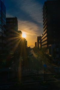 City street by buildings against sky during sunset