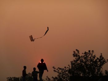 Family flying kite against orange sky during sunset