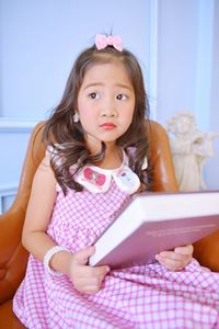 Cute girl reading book while sitting on sofa at home